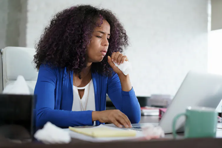A woman coughing at her desk.
