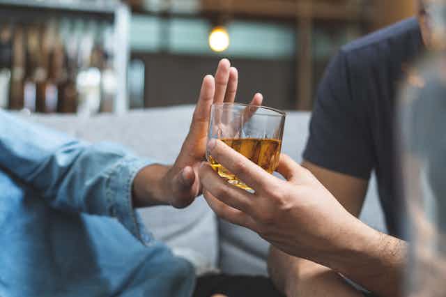 A person's hand pushing away another person's hand that is holding a glass of whisky