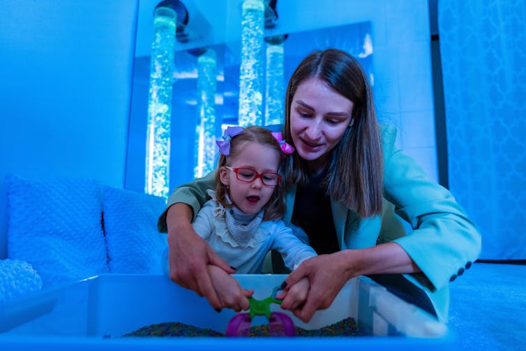 woman helps small child with disability in blue room