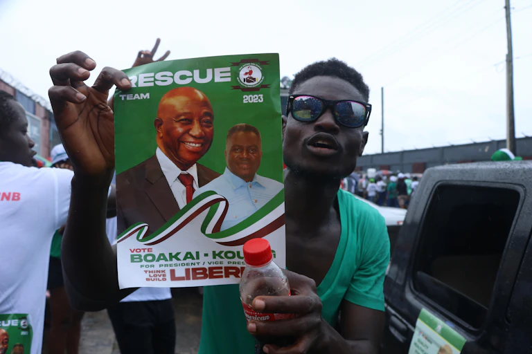 A man in a green T-shirt holds a poster promoting Boakai.
