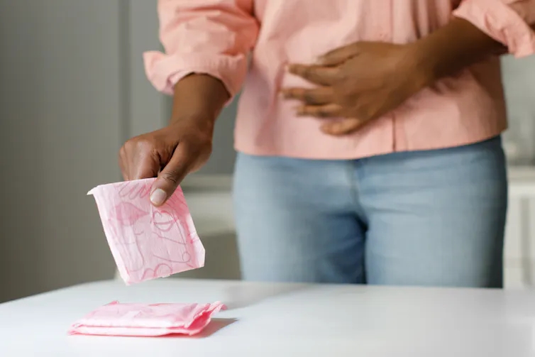 A woman with her period picks up a pink pad from a table.