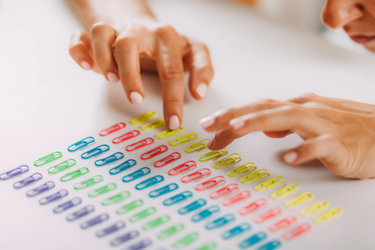 Woman ordering paper clips by colour in neat rows