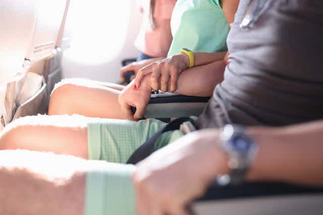 Woman anxiously holding man's forearm on an airplane
