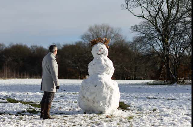 Man looks at snowman in park