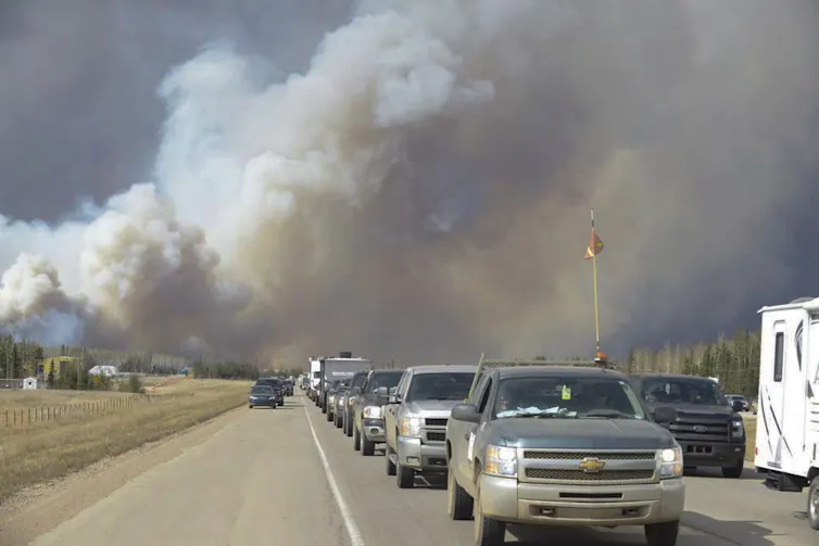 a line of cars driving away from billowing smoke
