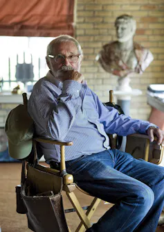 A man in a blue shirt seen sitting in a director's chair.