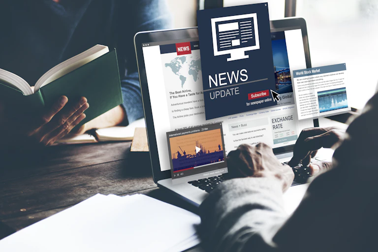 A news consumer calls up content on a laptop as another person reads a book.