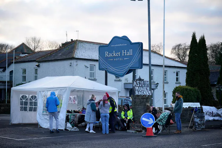 Protestors mingle outside a hotel next to a marquee with refreshments/
