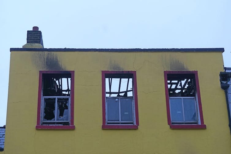 The blown out top floor windows of a building with signs of smoke damage.