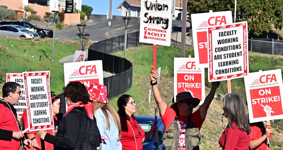 People in red clothing hold signs saying 'Union Strong' and 'California Faculty Association.'