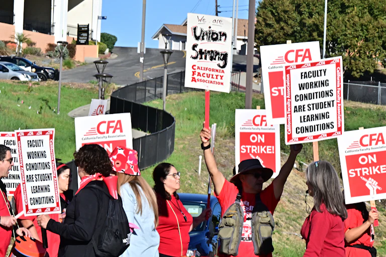 People in red clothing hold signs saying 'Union Strong' and 'California Faculty Association.'