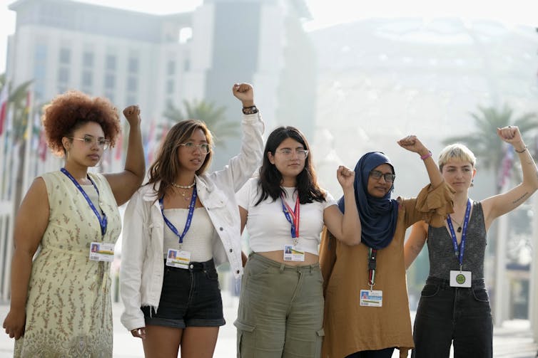 Five women stand in a row with their fists held high.