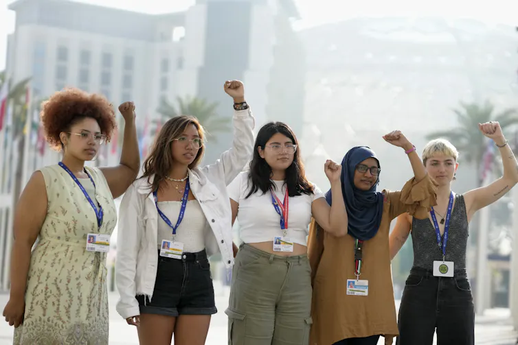 Five women stand in a row with their fists held high.