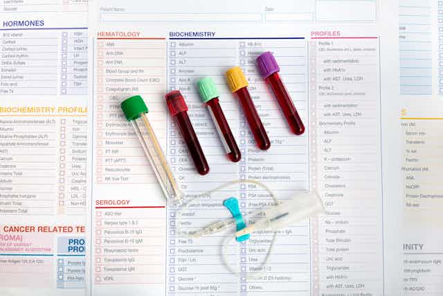 Four full and one empty heparin tubes and a butterfly needle arrayed on a checklist of blood test measurements
