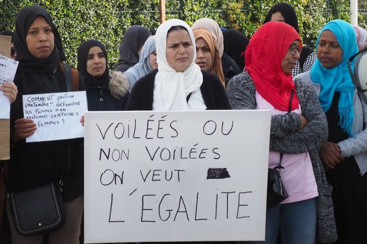 About half a dozen women in headscarves look frustrated as they hold signs on the street.