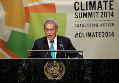 A man in a suit speaking at a podium with the UN logo. He stands in front of a sign reading Climate Summit 2014