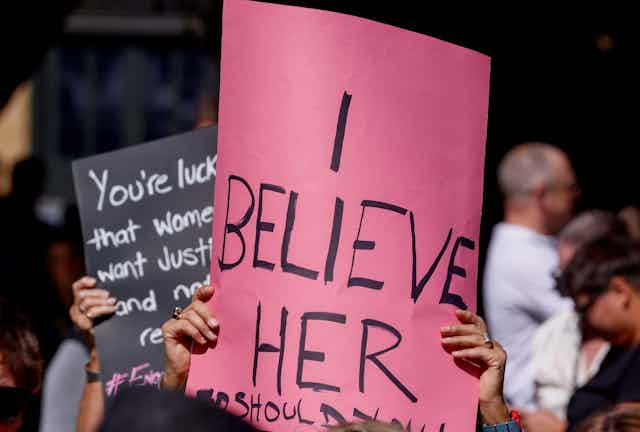 A pink sign that reads 'I believe her'