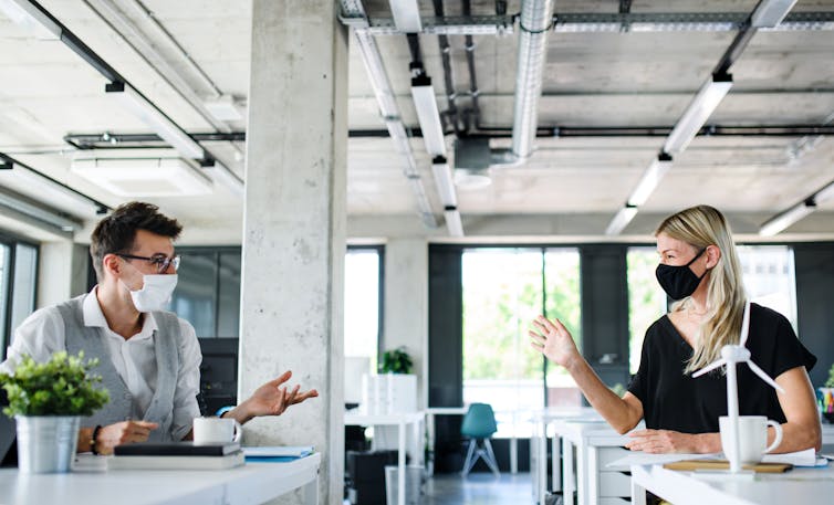 Two people wearing masks in an office.