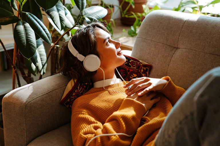 Brunette young woman listening music while resting on couch at home