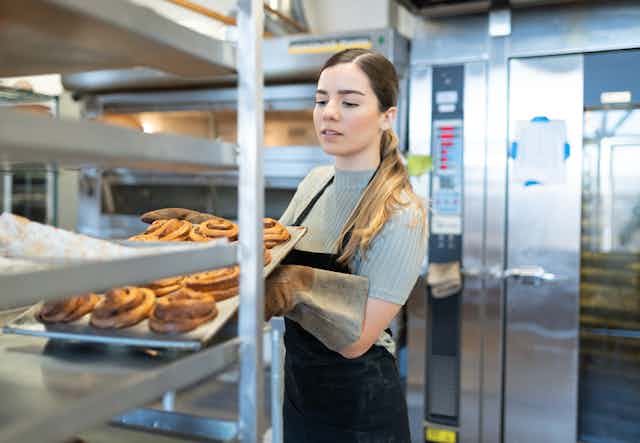 Young bakery worker tipping tray of pastries onto a cooling rack