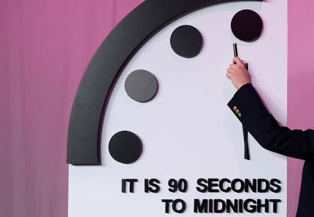A hand moving a clock hand to 90 seconds to midnight