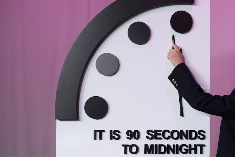 A hand moving a clock hand to 90 seconds to midnight