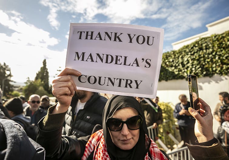A woman in a crowd ,carries a sign saying: 'Thank you, Mandela's country'.