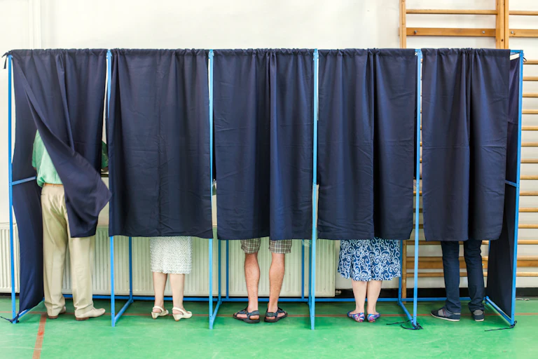 Color image of some people voting in some polling booths at a voting station.