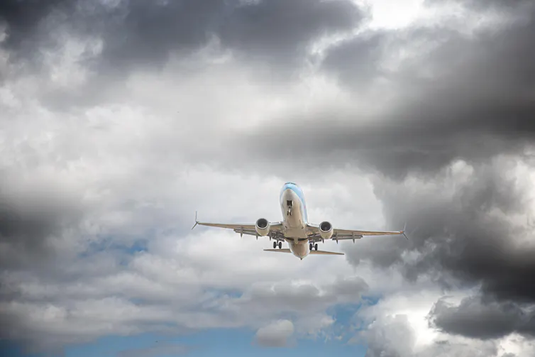 A plane flying under dark clouds.