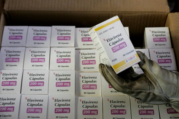 Gloved hand taking a pack of medication labelled Efaviernz 200mg from a box containing many packs of the drug