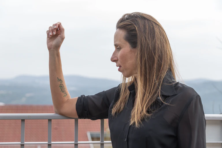 A woman in a black shirt holds up her arm on which there is a tattooed number.