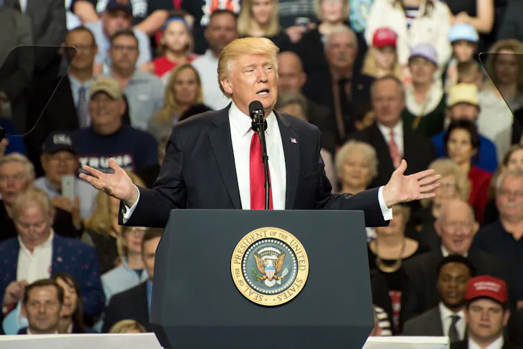 Donald Trump with his arms outstretched addressing a crowd at a rally.