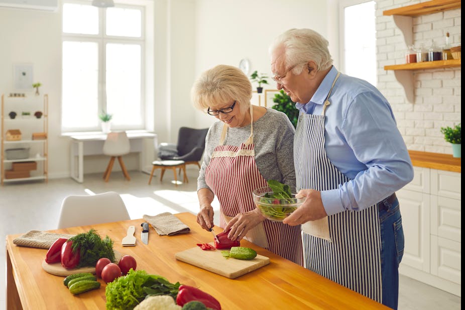 An elderly couple chop fresh vegetables for a salad.