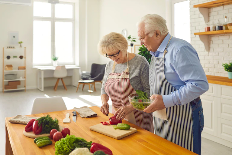 An elderly couple chop fresh vegetables for a salad.