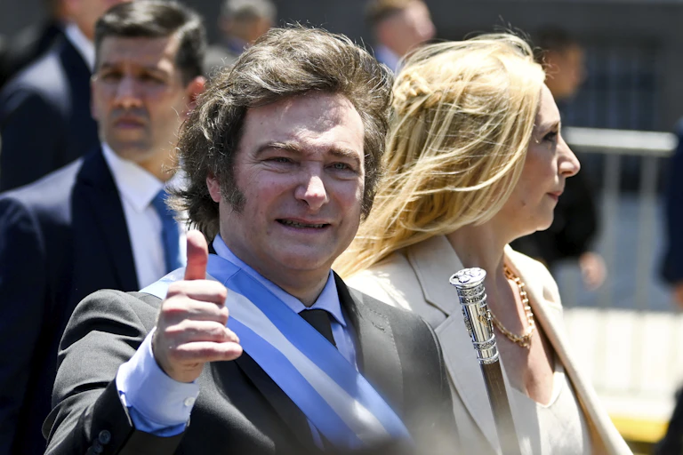 Man with long hair holds thumb in the air accompanied by blonde woman