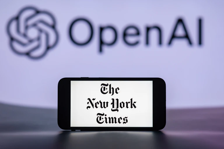 In a photo illustration, a mobile phone displays the logo of The New York Times, with that of OpenAI in the background.