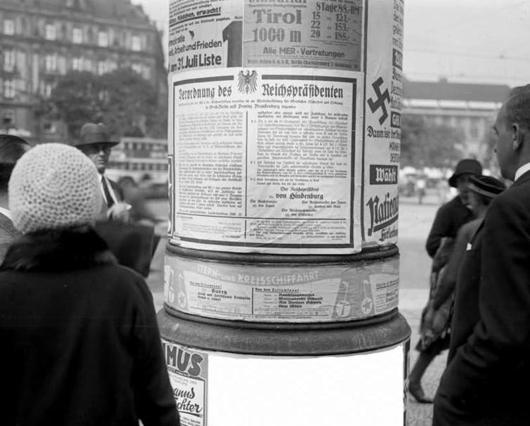 A woman and a man read a poster glued to a post.