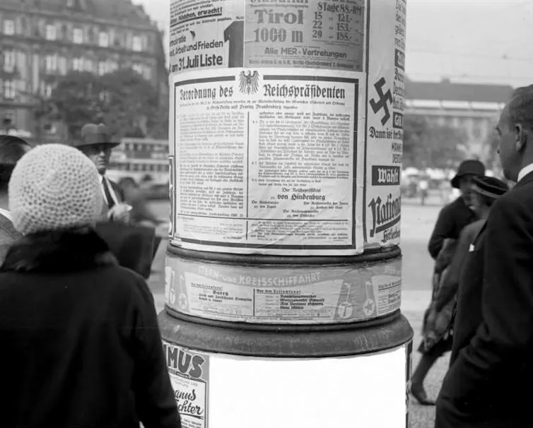 A woman and a man read a poster glued to a post.