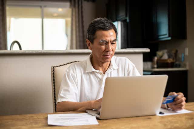a man sits at a table in front of a laptop computer while holding a credit card