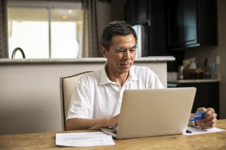a man sits at a table in front of a laptop computer while holding a credit card
