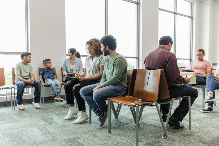 A multiracial group of people fill out their paperwork in the doctor's waiting room.