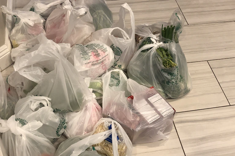 Large pile of white plastic bags filled with groceries sitting on tile floor.