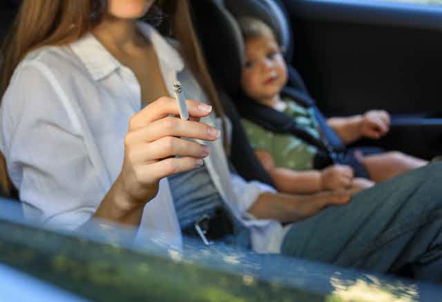 Madre fumando en el coche cerca de su hijo pequeño