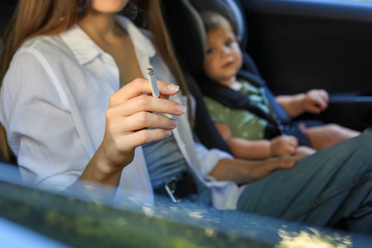 Madre fumando en el coche cerca de su hijo pequeño