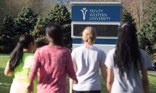 Four students in T-shirts walk towards a sign reading Trinity Western University.