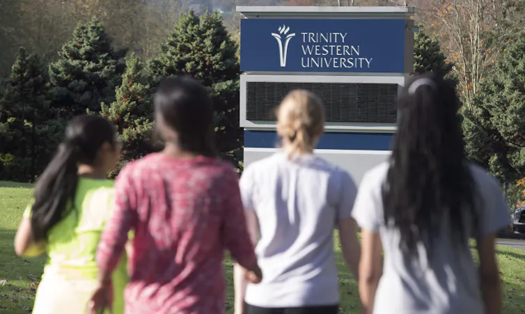 Cuatro estudiantes con camisetas caminan hacia el letrero de Trinity Western University.