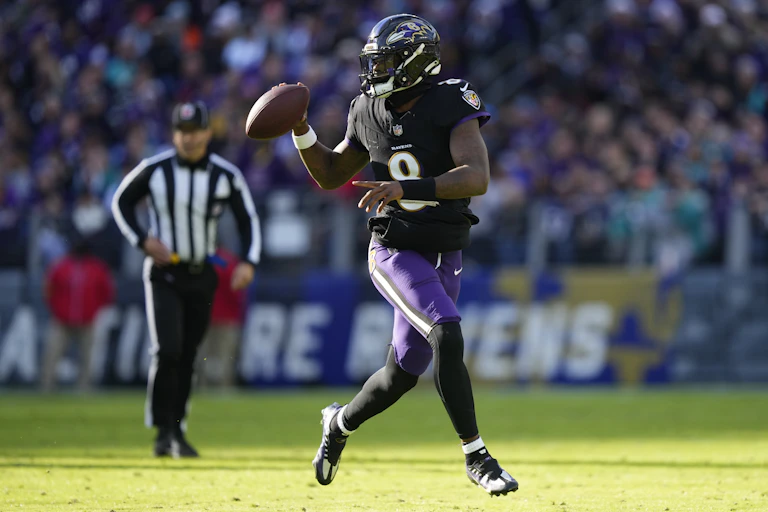 A Black man in a football uniform run down a football field while holding a football