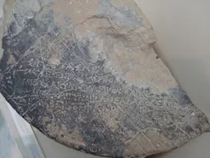 A weathered piece of stone with ancient Greek inscribed on the surface