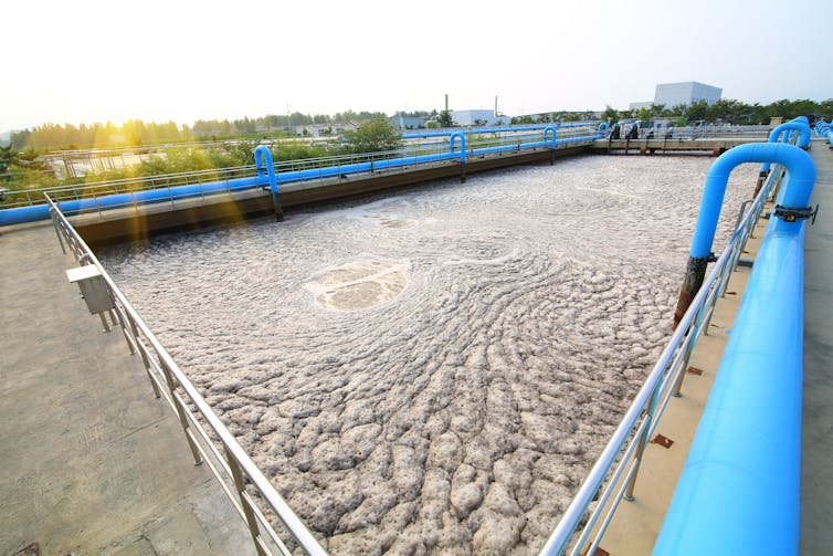 Sludge pours into a large open tank at a waste treatment plant