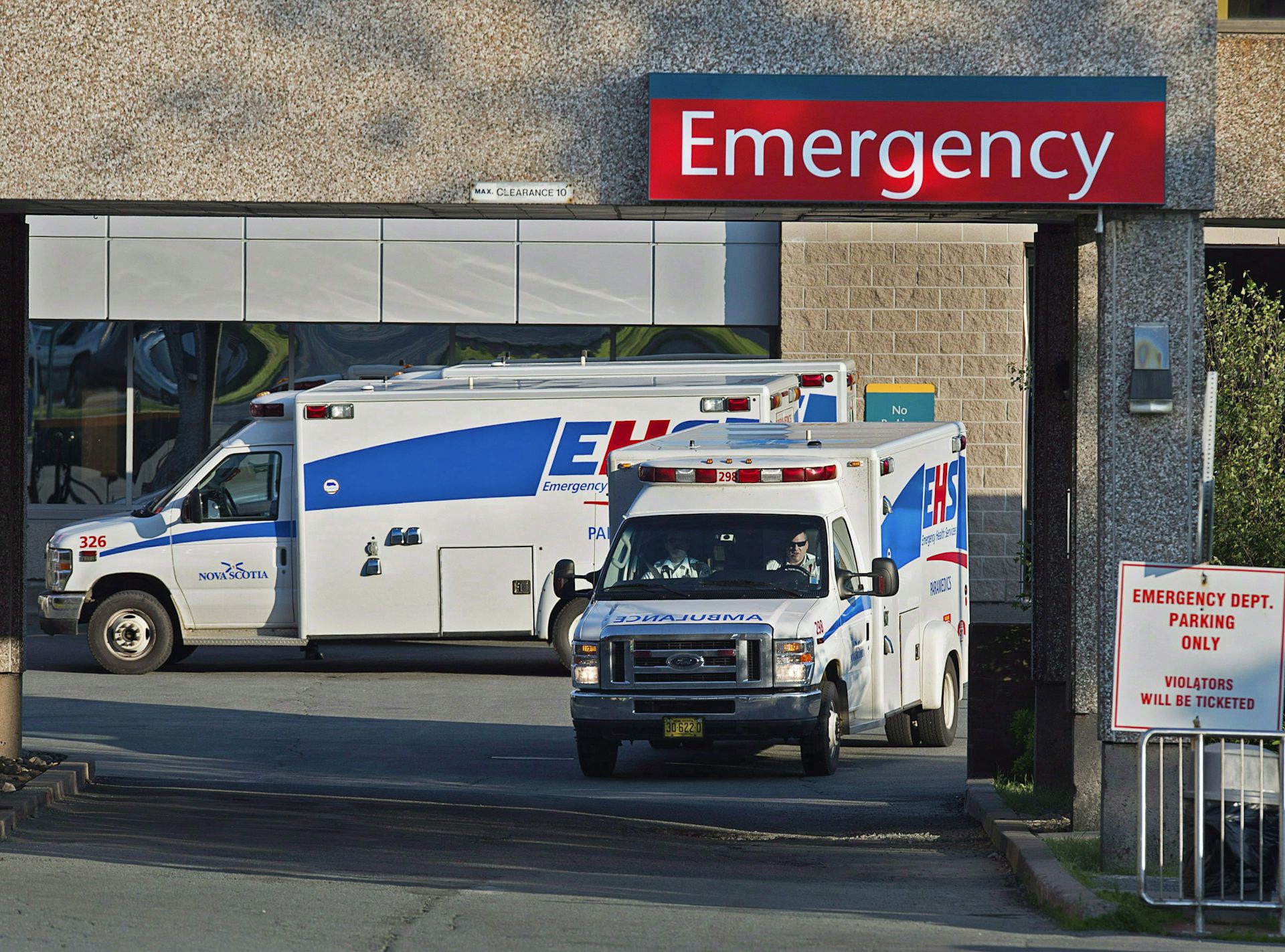 Two ambulances under a large red emergency sign.